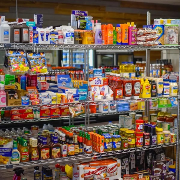 Shelves stocked with various grocery items, including condiments, snacks, and household goods at Gem Grill & Pizzeria.