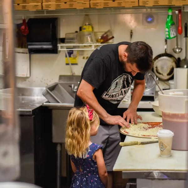 A chef and a young girl making a pizza together in a busy kitchen at Gem Grill & Pizzeria.