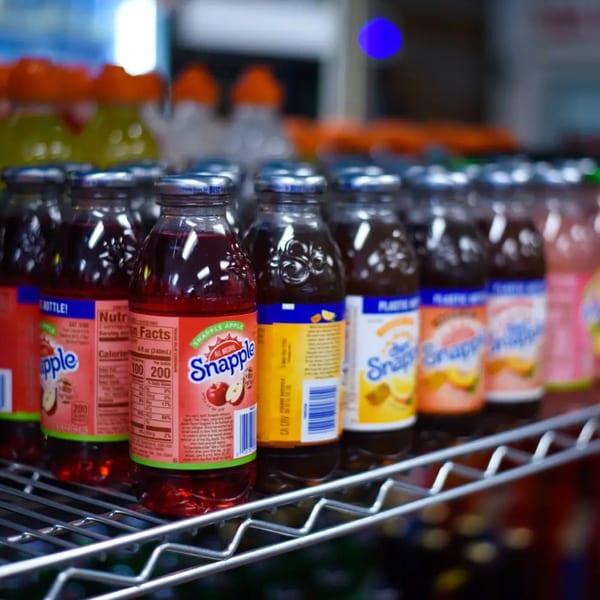 Rows of various Snapple drinks, including apple, peach, and lemon tea, on a metal shelf.